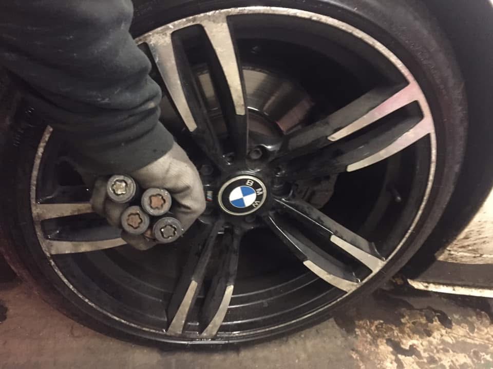 Set of removed locking wheel nuts held in front of a BMW alloy wheel